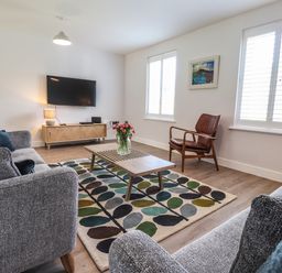A living room with grey sofas a wooden coffee table and a wall-mounted TV at Ty Owen in Newport Pembrokeshire