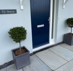 A blue front door with two potted topiary trees on either side and a sign reading Ty Owen on a white textured wall at Ty Owen Newport Pembrokeshire