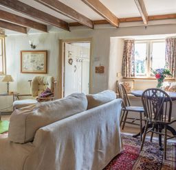 A sitting room with a sofa chair a table with flowers and exposed wooden beams at End Cottage in Malborough