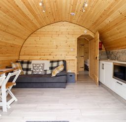 A curved wooden room with a sofa a small dining table with chairs and a kitchenette with microwave at Meadow Lodge @ Berrys Place Farm in Churcham