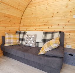 A gray sofa with plaid pillows and a throw in a wooden paneled room at Meadow Lodge at Berrys Place Farm in Churcham