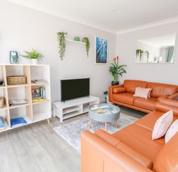 A living room with orange leather sofas a TV on a white stand a white shelving unit with baskets and books and plants at Mermaid House in Brewers Quay Harbour