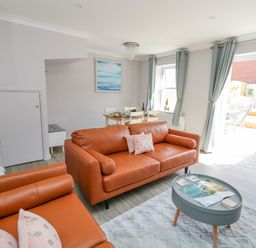 A living room with two orange sofas a blue coffee table and a dining table with chairs by windows and curtains at Mermaid House in Brewers Quay Harbour