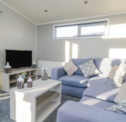 A living room with a blue sectional sofa a coffee table with vases a television on a stand and patterned curtains at Yealand 36 in Tewitfield