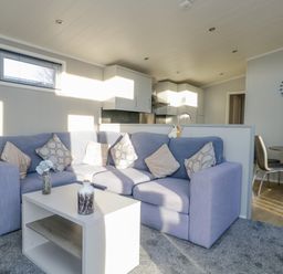 A living room with a blue sofa a white coffee table and a dining area with chairs at Yealand 36 in Tewitfield
