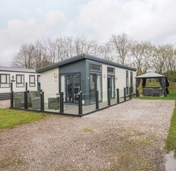 A modern single-story cabin with glass patio fencing and a gazebo with seating at Yealand 36 in Tewitfield