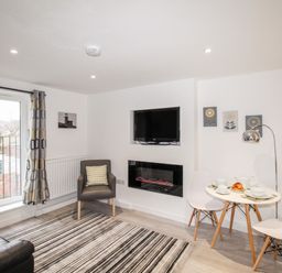 A living room with a black leather sofa striped rug armchair wall-mounted TV and a small dining table with white chairs at Portside in Greenhill Weymouth