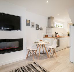 A kitchen and dining area with a mounted television, electric fireplace, round table with two chairs, and kitchen appliances at Portside Greenhill Weymouth