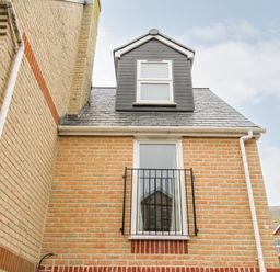 A brick exterior wall with a window and metal railing and a dormer window on the roof at Portside in Greenhill Weymouth