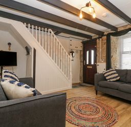 A living room with two sofas a round rug a mounted TV stairs and a wooden door at Walter in Newlyn