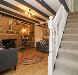 A living room with a stone fireplace two grey sofas a round rug wooden floor and stairs with carpet at Walter in Newlyn