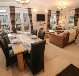 A dining area with a table set for six and a living room with two brown sofas and a wall-mounted tv at 16 Heritage Park Heritage Park near Kilgetty