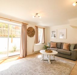 A living room with a gray sofa pillows a white round coffee table rug and sliding glass doors at Amaranta Brewers Quay Harbour