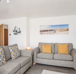 A living room with two grey sofas and patterned cushions and a beach picture on the wall at 31 Beach Road in Morfa Bychan
