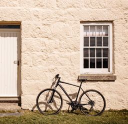 A black bicycle leaning against a stone wall next to a closed white door and a window with white frames