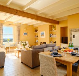 A living room with sofas a coffee table a dining table set with plates and glasses and a window with curtains at Higher Roskestal St Levan near Porthgwarra