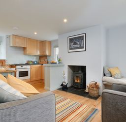 A living room with a fireplace a kitchen with wooden cabinets and a dining table at Corner Cottage in Porthgwarra