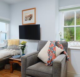 A sitting area with a gray armchair and a daybed near two windows at Corner Cottage in Porthgwarra