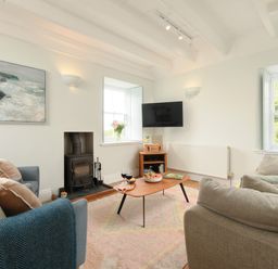 A living room with sofas cushions a coffee table a television and flowers at Cove Cottage in Porthgwarra