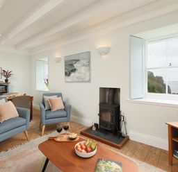 A living room with two blue armchairs a wood stove and a coffee table with fruit and wine at Cove Cottage in Porthgwarra