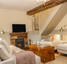 A living room with beige sofas a wooden coffee table a fireplace and a television at Omas Cottage in Moreton In Marsh