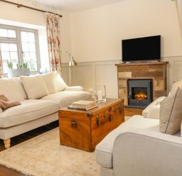 A living room with beige sofas and cushions wooden chest table and a fireplace with TV above at Omas Cottage Moreton-In-Marsh