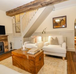 A living room with two armchairs a wooden chest coffee table a fireplace and a television at Omas Cottage in Moreton In Marsh