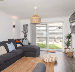 A living room with a dark sectional sofa cushions a striped floor pillow and a sliding glass door overlooking a garden at Dolwyn in Llandegfan