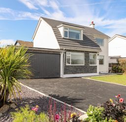 A detached house with a gray roof a double garage a driveway plants and flowers in the garden at Dolwyn in Llandegfan