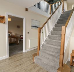 A hallway with carpeted stairs wooden banisters a wooden bench and a coat rack at Tan Twr in Llanfairpwll
