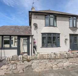 A two-story house with bay windows and a stone wall in front at Beeches Bach in Prestatyn