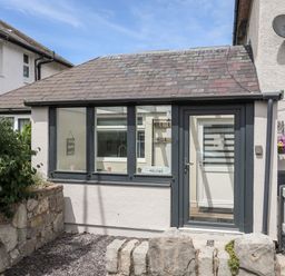 Small stone and slate roof house with glass door and windows and a low stone wall at Beeches Bach in Prestatyn