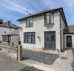 A two story house with bay windows and a stone wall at Beeches Bach in Prestatyn