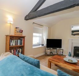 A living room with a wooden bookshelf a sofa with blue cushions a wooden coffee table a television and a fireplace at The Old Mill in Keswick