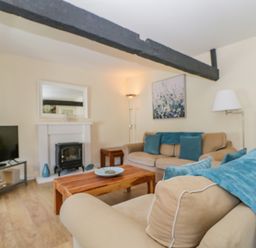 A living room with beige sofas and blue cushions a wooden coffee table a television and a fireplace at The Old Mill in Keswick