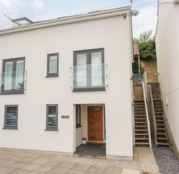 A modern white house with gray framed windows and a wooden door with stairs on the right at 3 Ty Stabal in Pwllheli