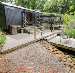 A shepherd's hut with decking and steps at The Shepherds Hut at Bridge Lake Farm & Fishery Chacombe