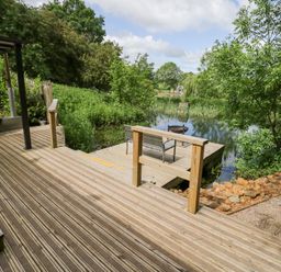 A deck overlooking a pond with seating at The Shepherds Hut at Bridge Lake Farm & Fishery Chacombe