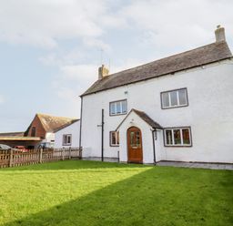 A white two-story house with a brown front door and multiple windows with a front lawn and a wooden fence at Ley Mill Farm in Huntley