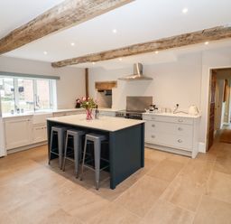 A kitchen with a central island and three stools under wooden ceiling beams at Ley Mill Farm in Huntley