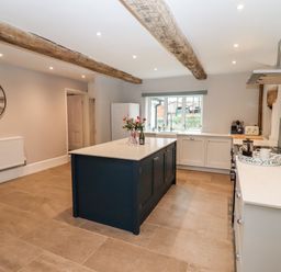 A kitchen with a central island, large wall clock, exposed wooden beams, and a window at Ley Mill Farm in Huntley