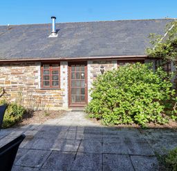 An outdoor view of a stone wall building with a door and pathway at Bracken Cottage St Tudy