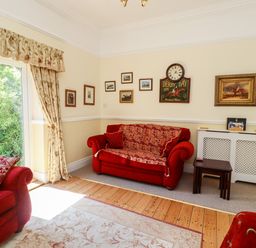 A living room with red sofas pictures on the walls and a door with curtains at Buzzards Rest in Stannington near Morpeth