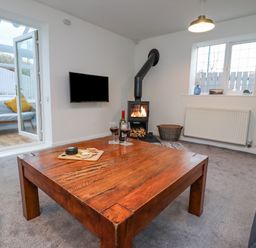 A living room with a wooden coffee table a wood stove a wall mounted tv and an open door to a sunroom at Pond Farm View in Hinderwell