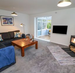A living room with a sectional sofa a wooden coffee table a wood stove and a wall-mounted television at Pond Farm View in Hinderwell