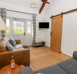A living room with two sofas a wooden side table a floor lamp a wall mounted tv and a sliding wooden door at Dryslwyn Cottage in Llandeilo