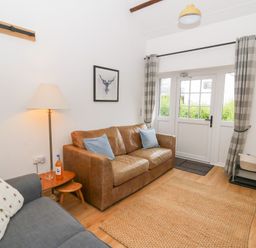 A sitting room with a brown leather sofa and a gray fabric armchair near a wooden floor lamp and a side table at Dryslwyn Cottage in Llandeilo