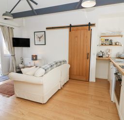 A living room with a sofa a wooden sliding door and a kitchen area with countertops and shelves at Dinefwr Cottage Golden Grove near Llandeilo