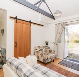 A living area with a sofa, armchair, sliding wooden door, and open double doors leading outside at Dinefwr Cottage Golden Grove near Llandeilo
