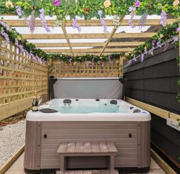 An outdoor hot tub under a wooden pergola decorated with flowers and greenery at The Stag - Crossgate Luxury Glamping Hartsop near Glenridding